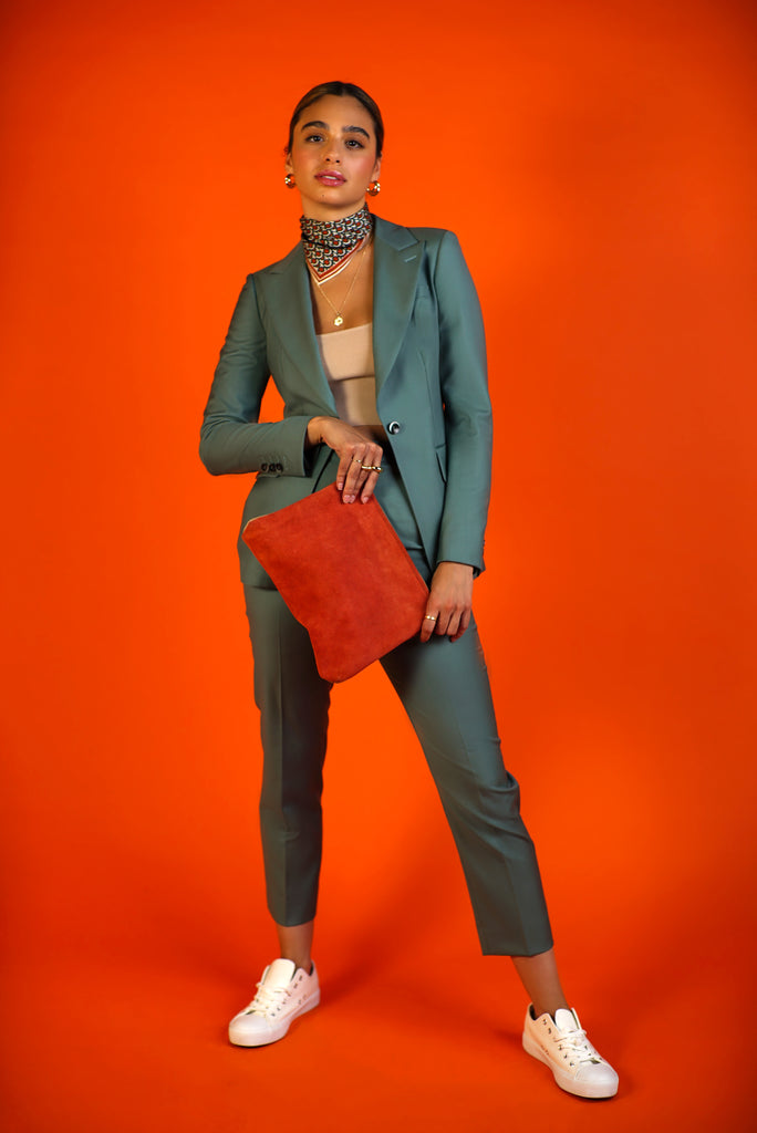 model posing in olive green suit peak lapels and cropped pant with orange suede clutch and silk scarf